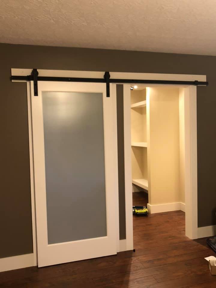 White sliding barn door with frosted glass on black track hardware in front of a walk-in closet